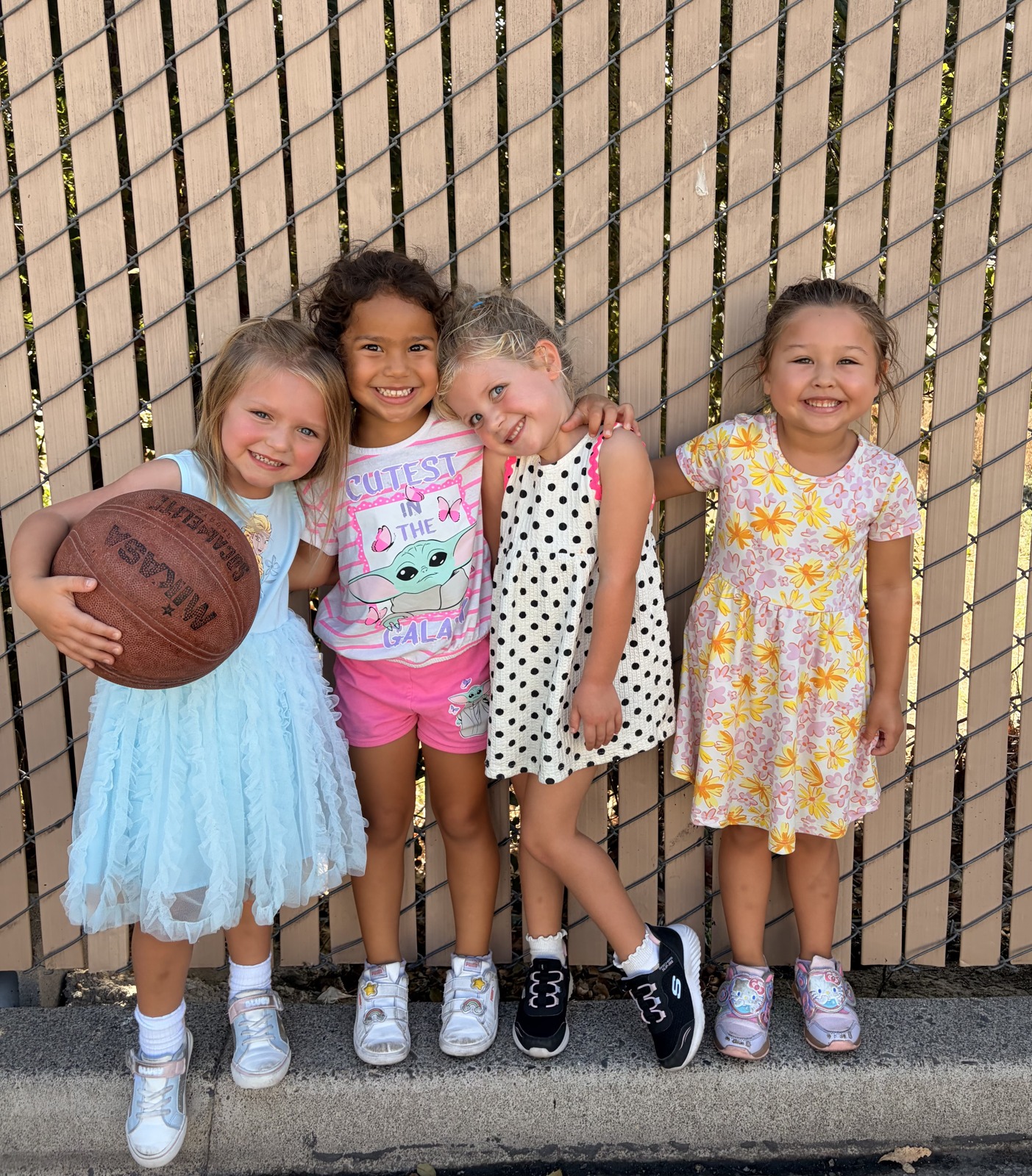 Four smiling children posing together in front of a fence at Happy Minds Kids Academy